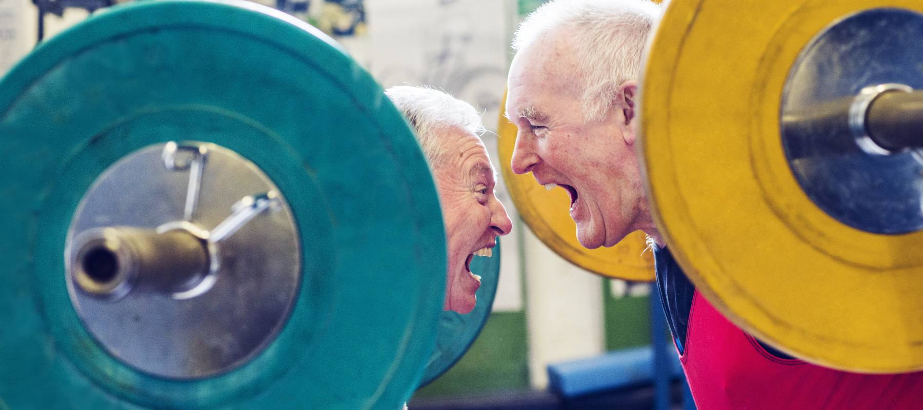 two Caucasian male seniors power lifting heavy weights, facing each other