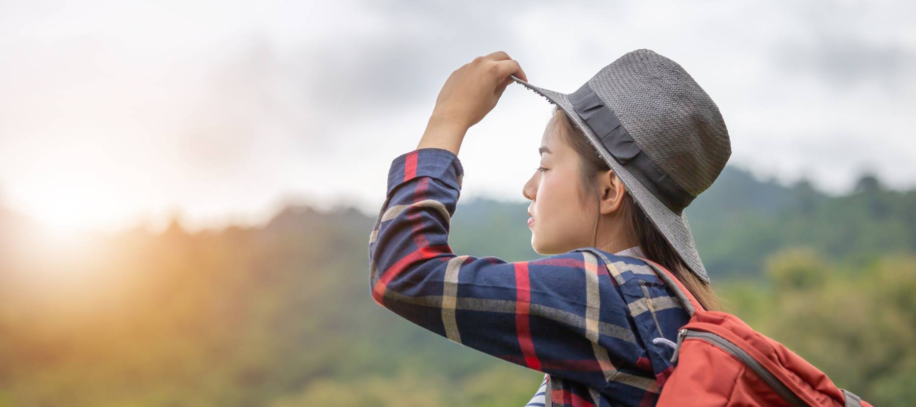 young Asian woman backpacking, eyes closed and facing toward the sunset