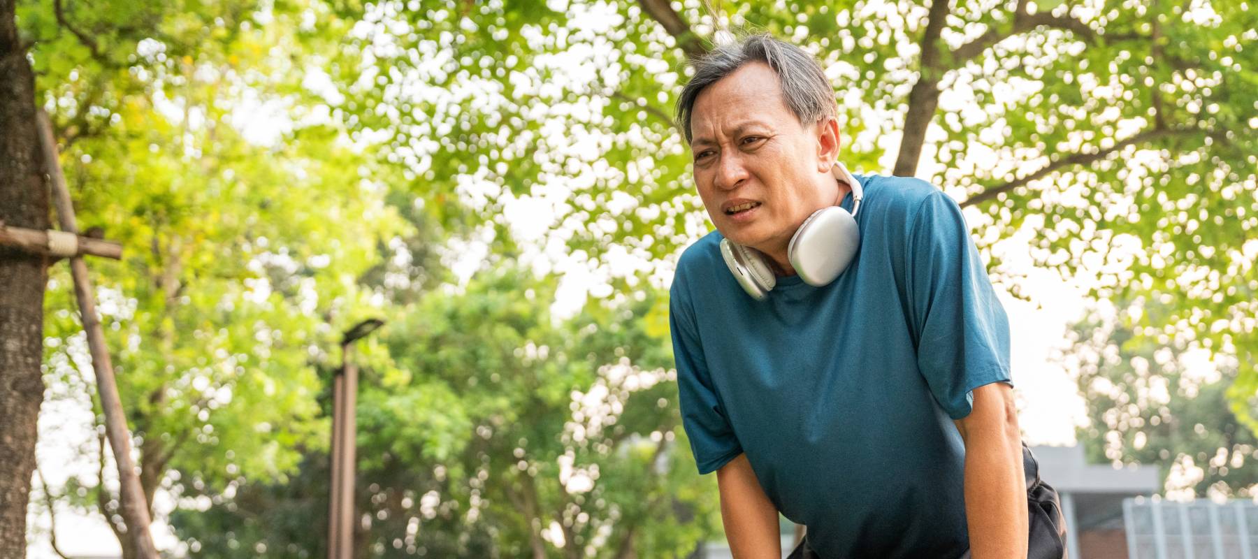 Older gentleman bending over following a jog with a thoughtful frown on his face.