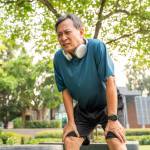 Older gentleman bending over following a jog with a thoughtful frown on his face.