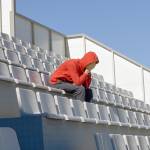 Fan sits in empty stands, hands over face sad