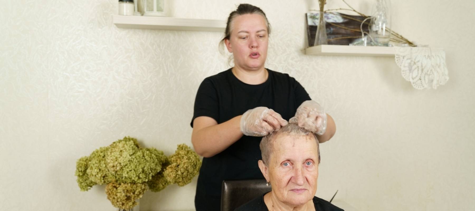 A woman daughter paints her elderly mother's hair with a brush