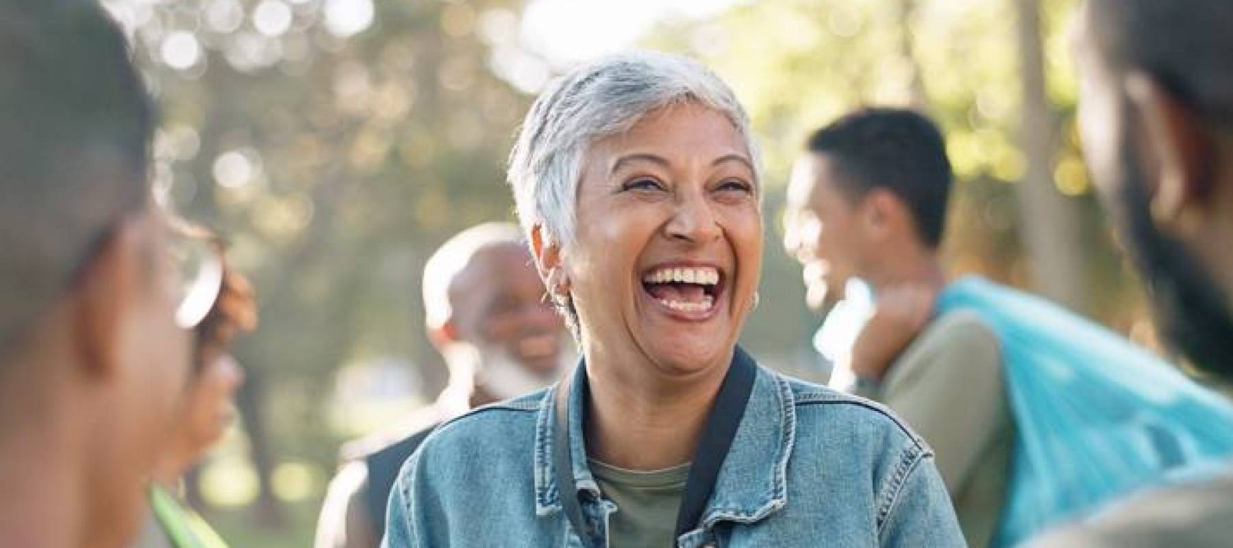 Woman with cropped white hair laughing with several other people.