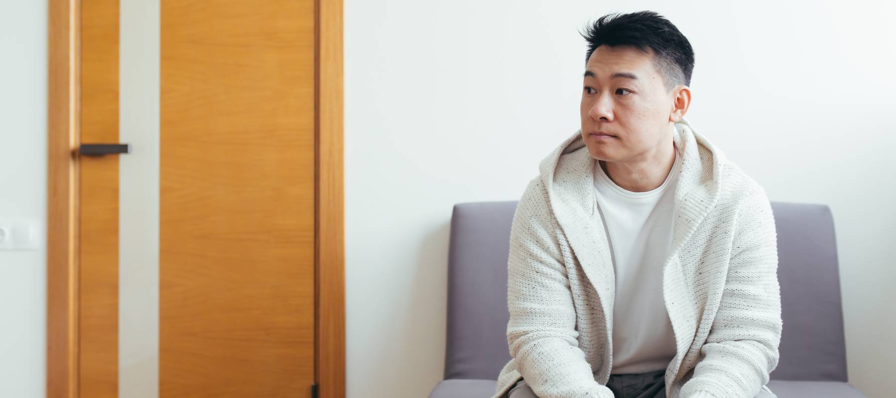 Asian man waits alone in waiting room looking concerned.