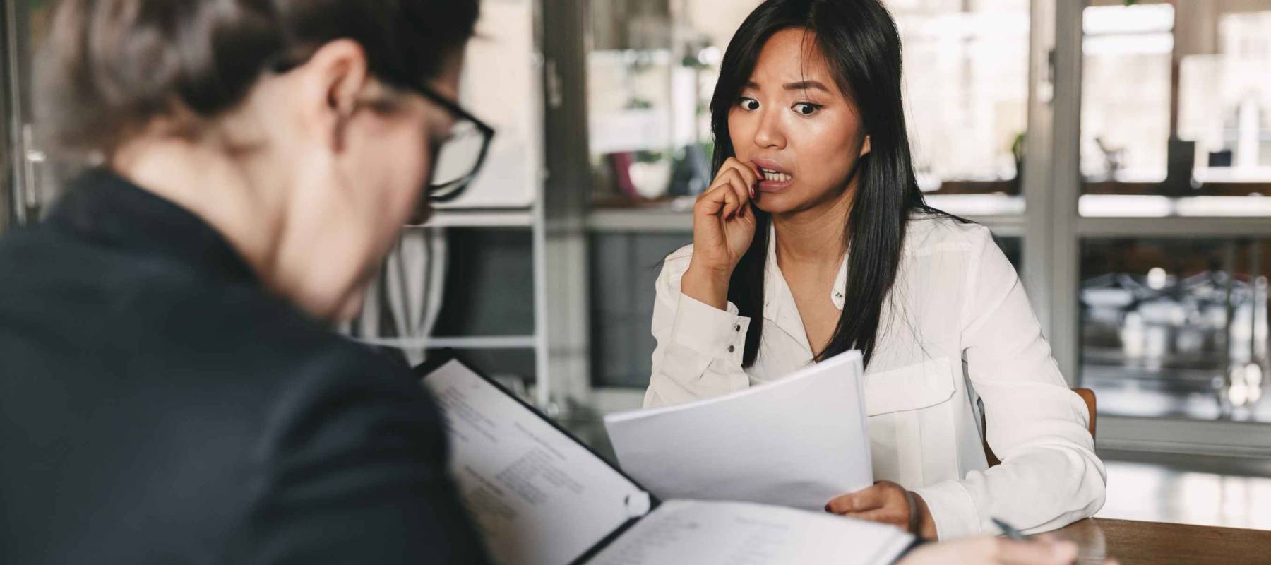 Photo from back of businesswoman interviewing and reading resume of nervous female applicant during job interview - business, career and placement concept