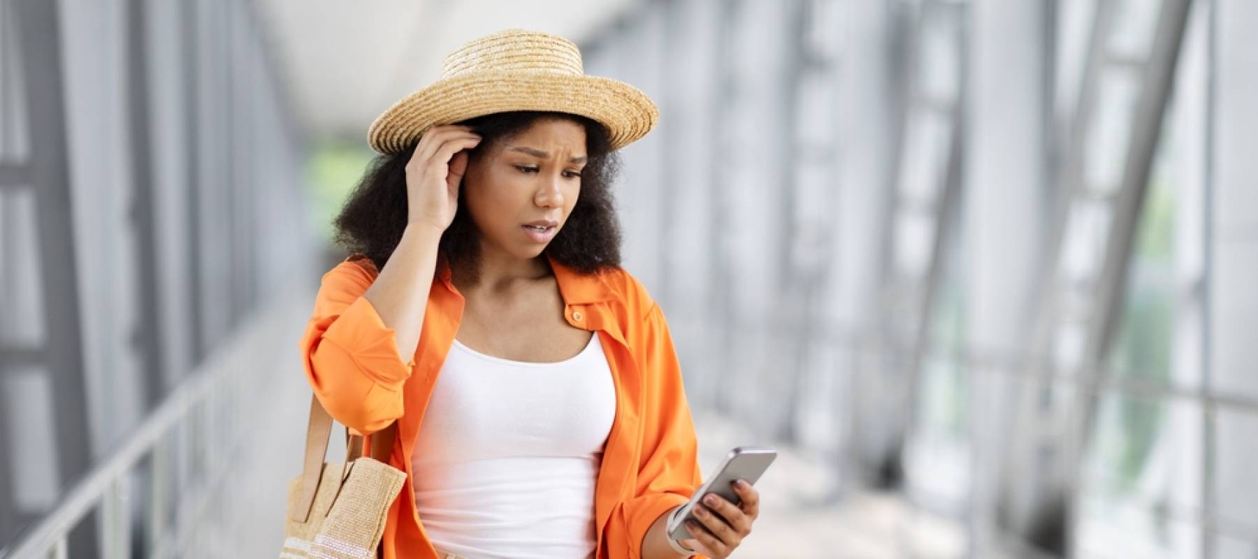 a young Black woman in an airport, looking at her phone with concern