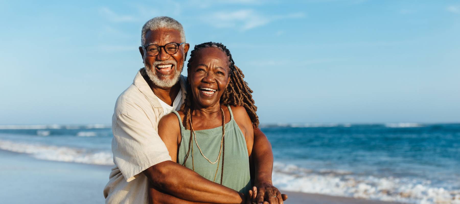 a Black couple in their 50s hugging and smiling at the camera on the beach