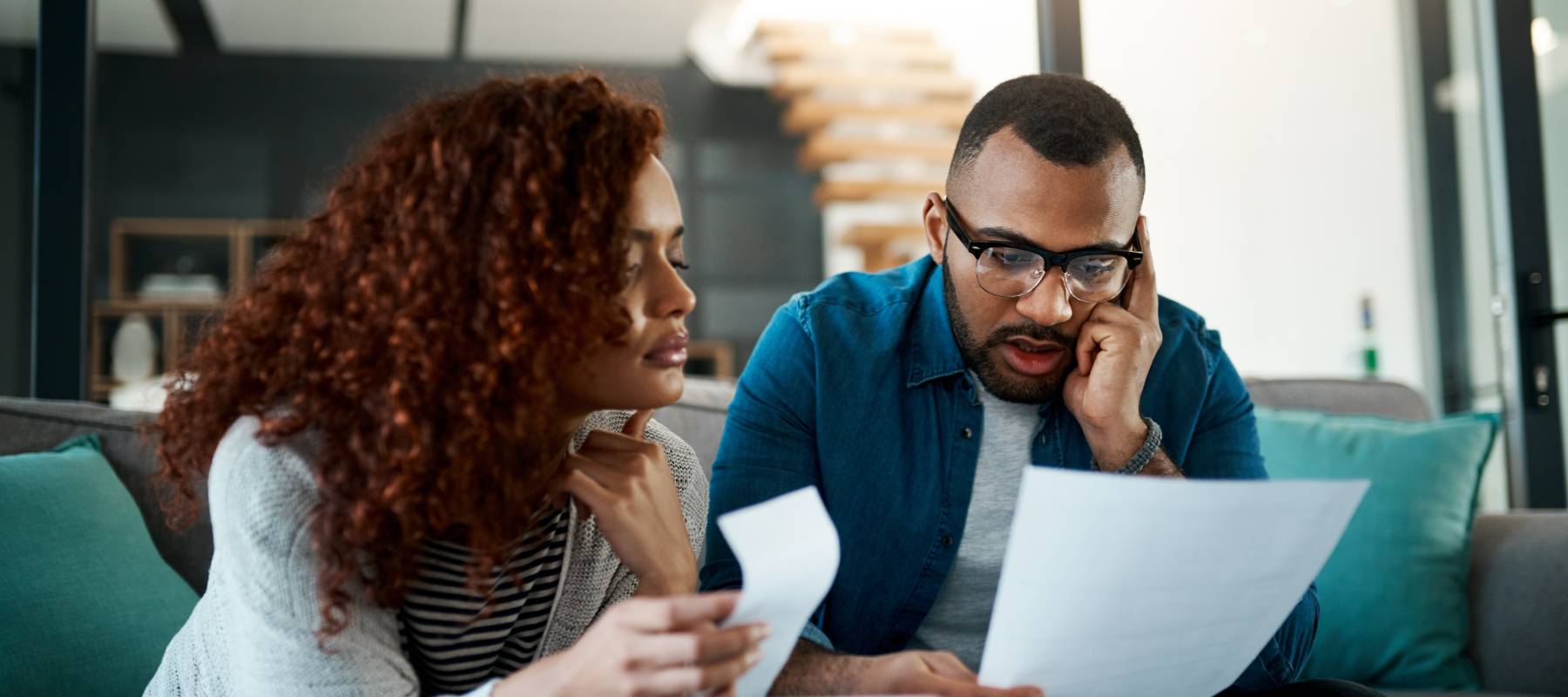 a young Black couple at home looking upset at some paperwork