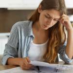Indoor shot of casually dressed young woman holding papers in her hands, calculating family budget.