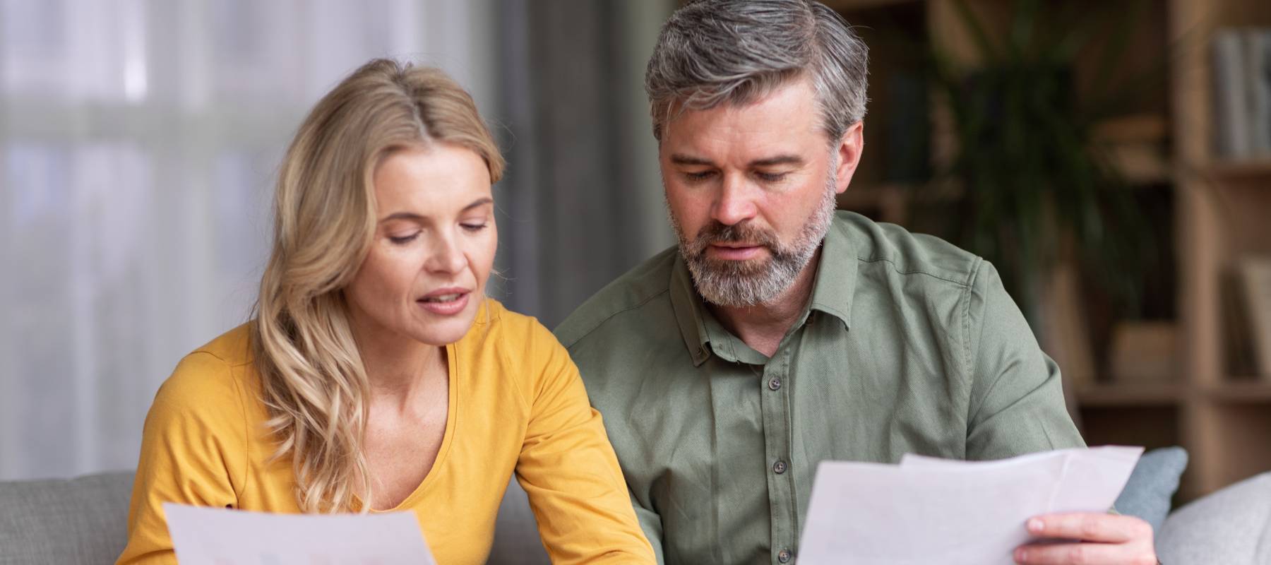 Busy middle-aged couple reviews and discusses their finances on a couch in a home setting.