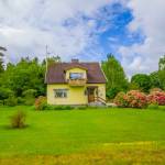 little yellow house with lots of greenery around, blue skies with clouds in the background