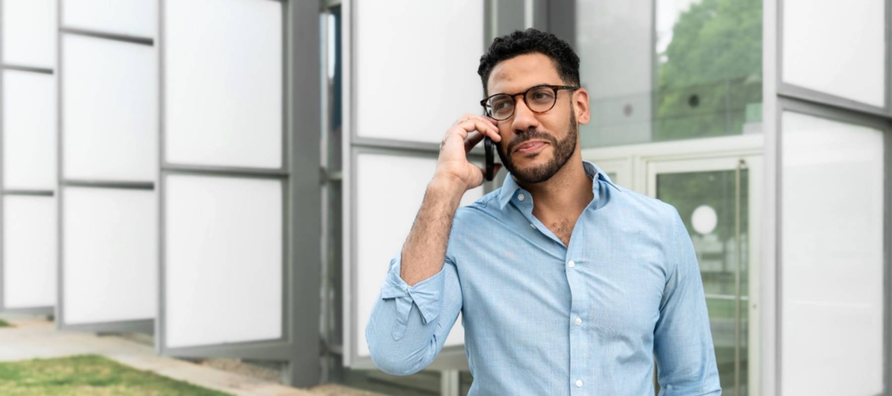Hispanic man in his 40s looking concerned while talking on his phone outside an office building