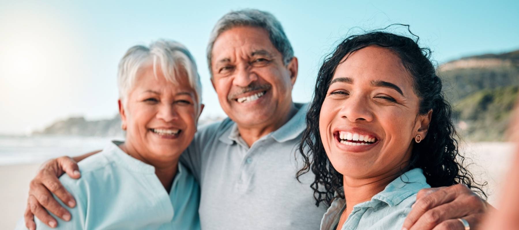 older parents with adult daughter smiling for a family photo on the beach
