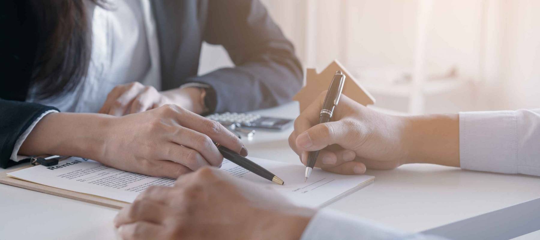 man signs a document on a clipboard, while woman across the table points at page with pen
