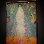 A collage image of Gustav Klimt in a loose fitting smock, beared and with a mostly shaved head, staring across the his iconic painting: the Portrait of Elisabeth Lederer.