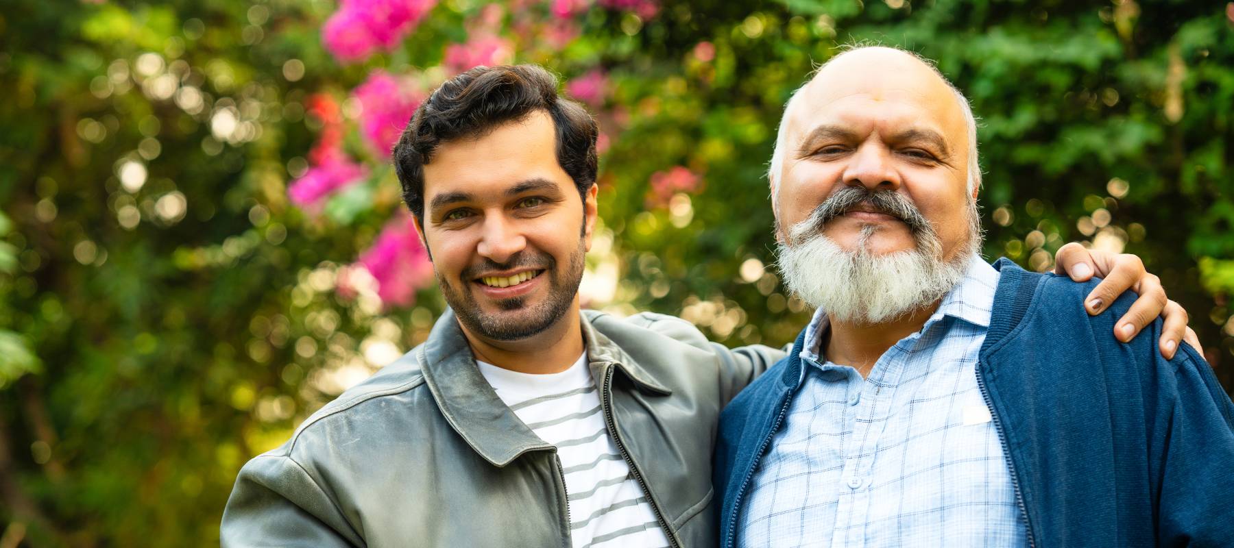 Indian father and young adult son walking in a home garden with coffee