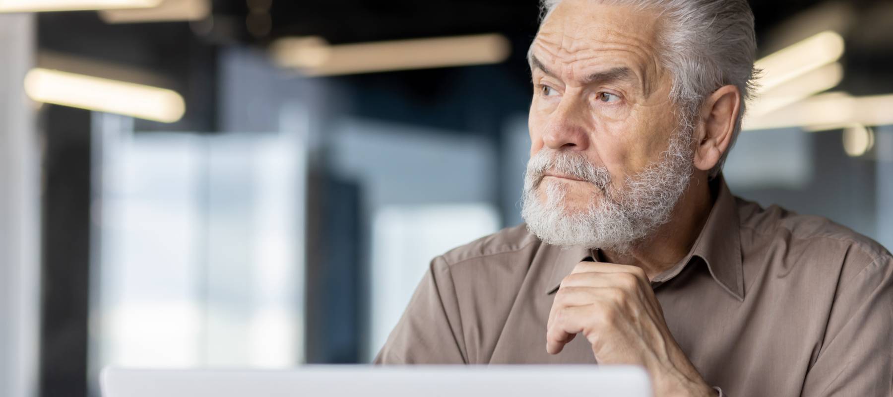senior Caucasian businessman deep in thought in a modern office setting with a laptop