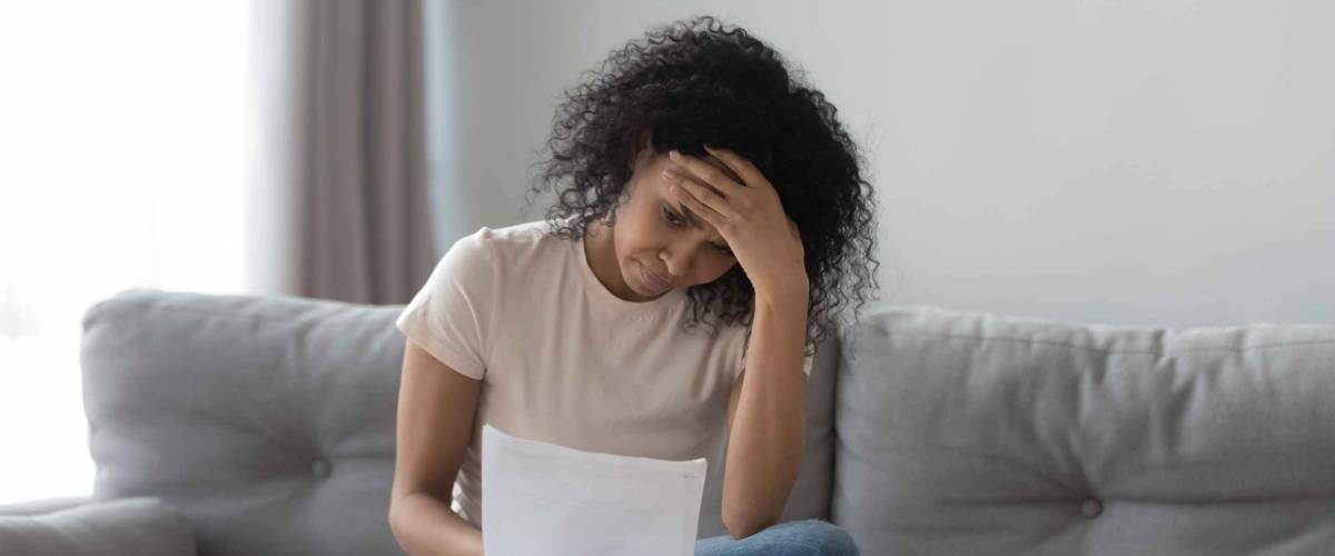 Stressed african woman holding papers sitting on sofa