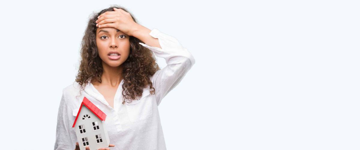Young hispanic real state agent woman holding small house stressed with hand on head, shocked with shame and surprise face, angry and frustrated. Fear and upset for mistake.