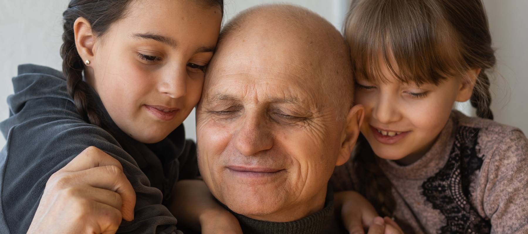 Older man hugging his tow female grandchildren.