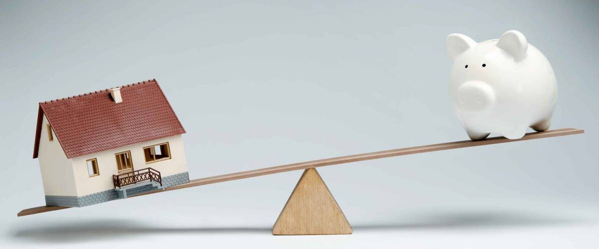 Home loans market. Model house and piggy bank balancing on a seesaw