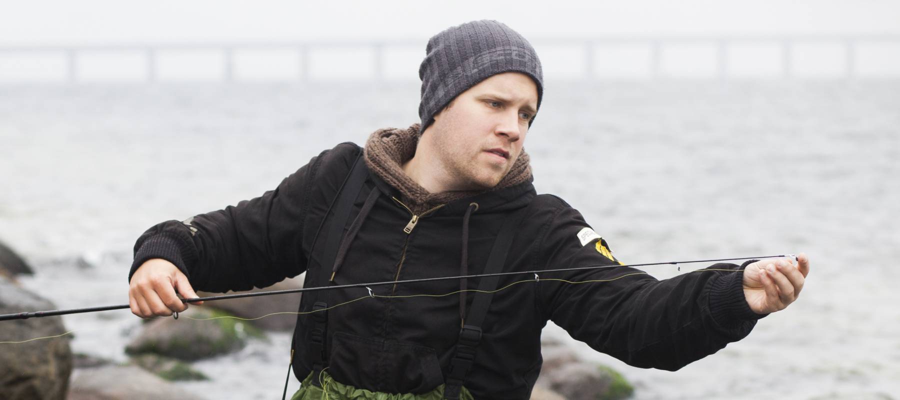 Worried man repairing fishing rod while standing in lake by rocks