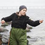 Worried man repairing fishing rod while standing in lake by rocks
