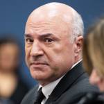Kevin O'Leary looks askew at the camera in a black suit, black tie and white shirt with a deep expression of concern.