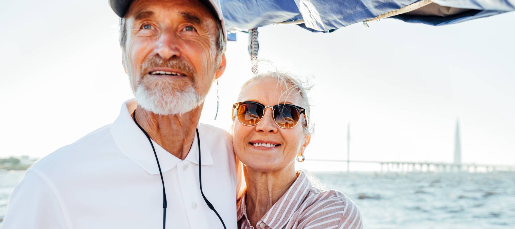 senior Caucasian couple tanding on sailboat at steering wheel and embracing each other