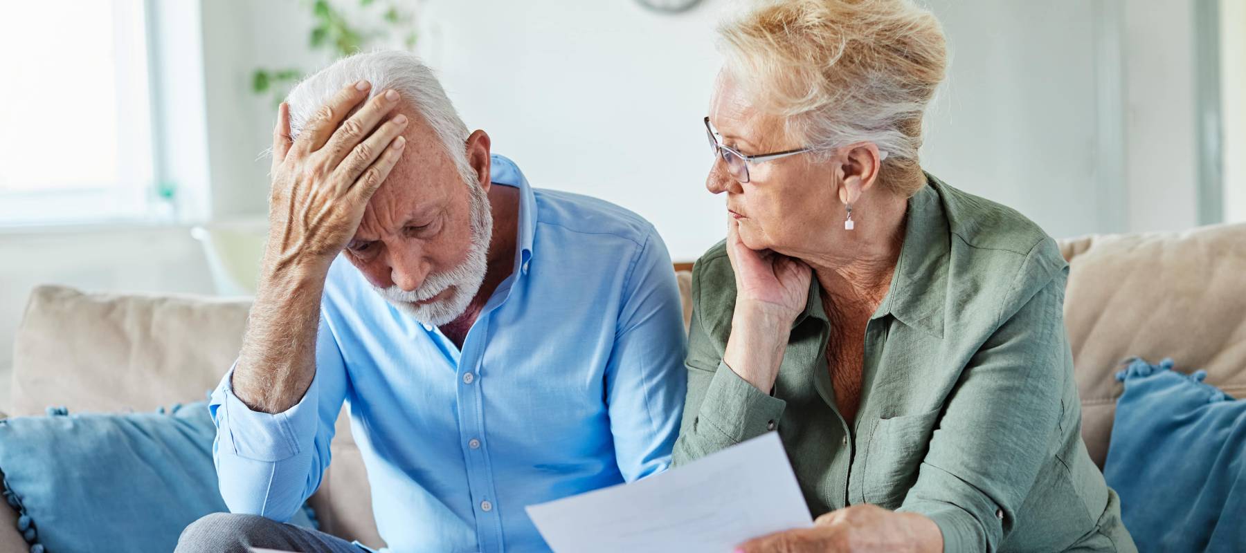 a Caucasian senior couple looking concerned and holding paperwork at home