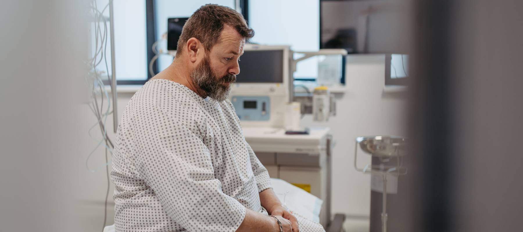 Man in hospital gown waiting for medical examination in hospital setting, looking anxious.
