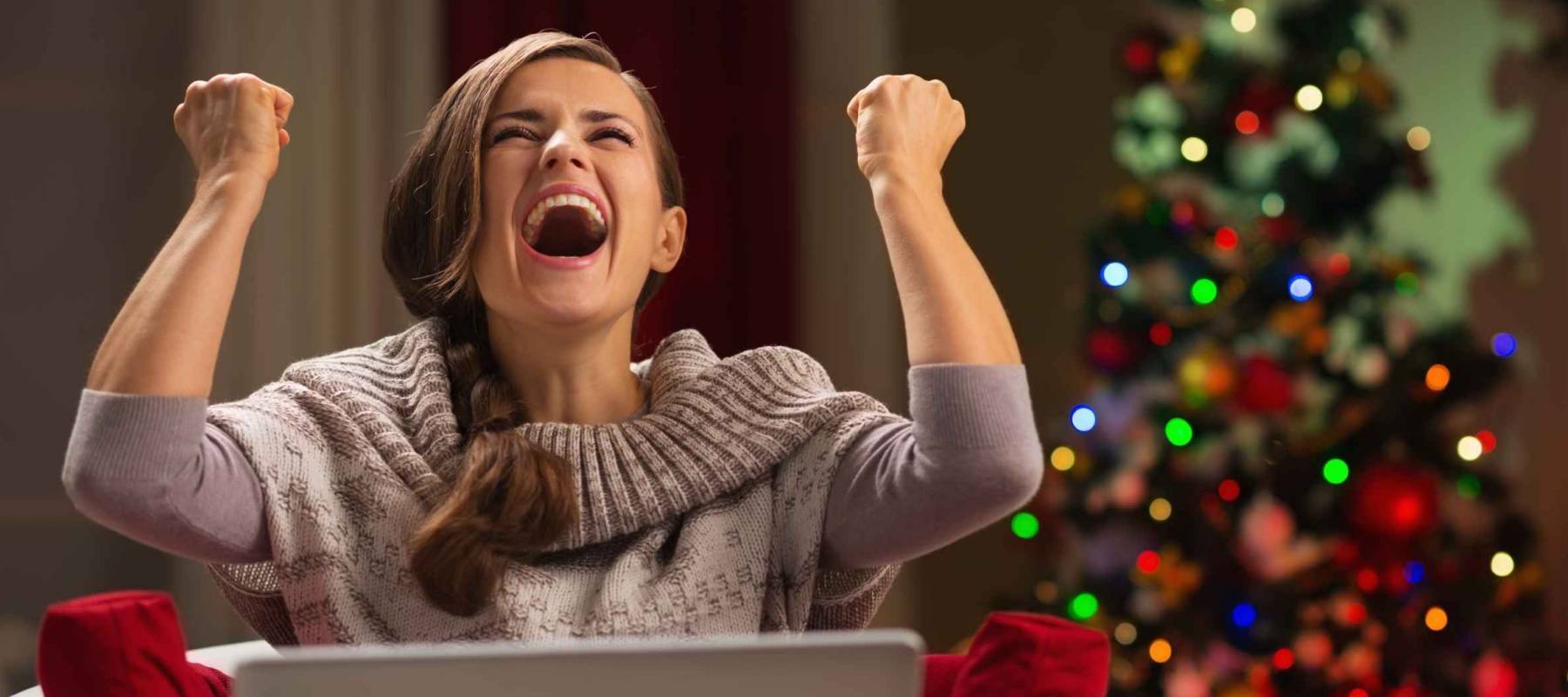 Happy woman with laptop rejoicing success in front of Christmas tree