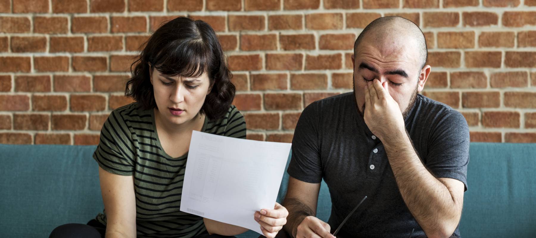 a young Caucasian couple looking concerned as they go over finance on their living room couch