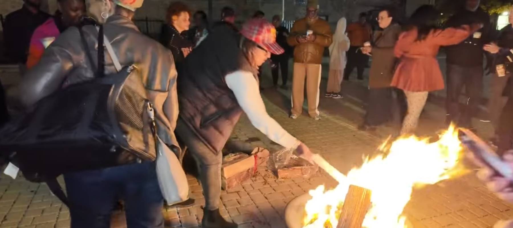 A crowd of North Lawndale residents gather around a roaring fire on a hardscaped patio to burn their property tax bills.