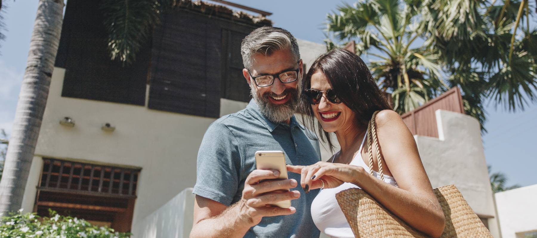 a middle-aged couple smiling and looking at a phone with a property listing