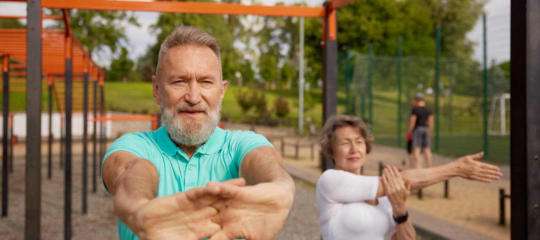 senior couple stretching arms before exercise at training field outdoors