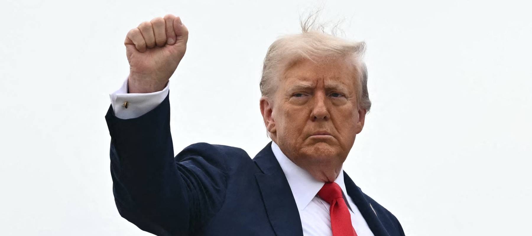 President Donald Trump board a plane high right hand raised in a fist, as if celebrating a victory.