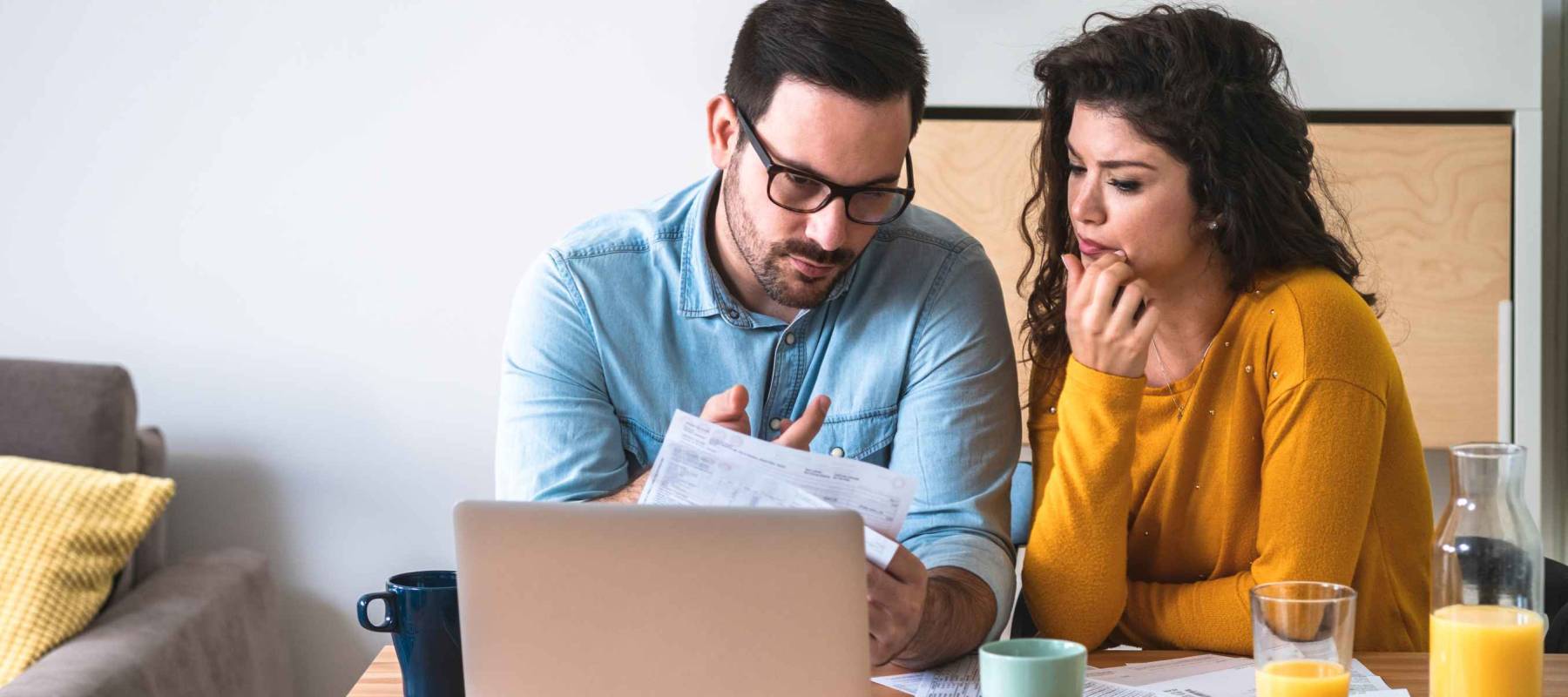 Worried couple looking at their bills at kitchen table with an open laptop