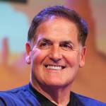 Mark Cuban smiles at the camera in a black zip up athletic shirt.