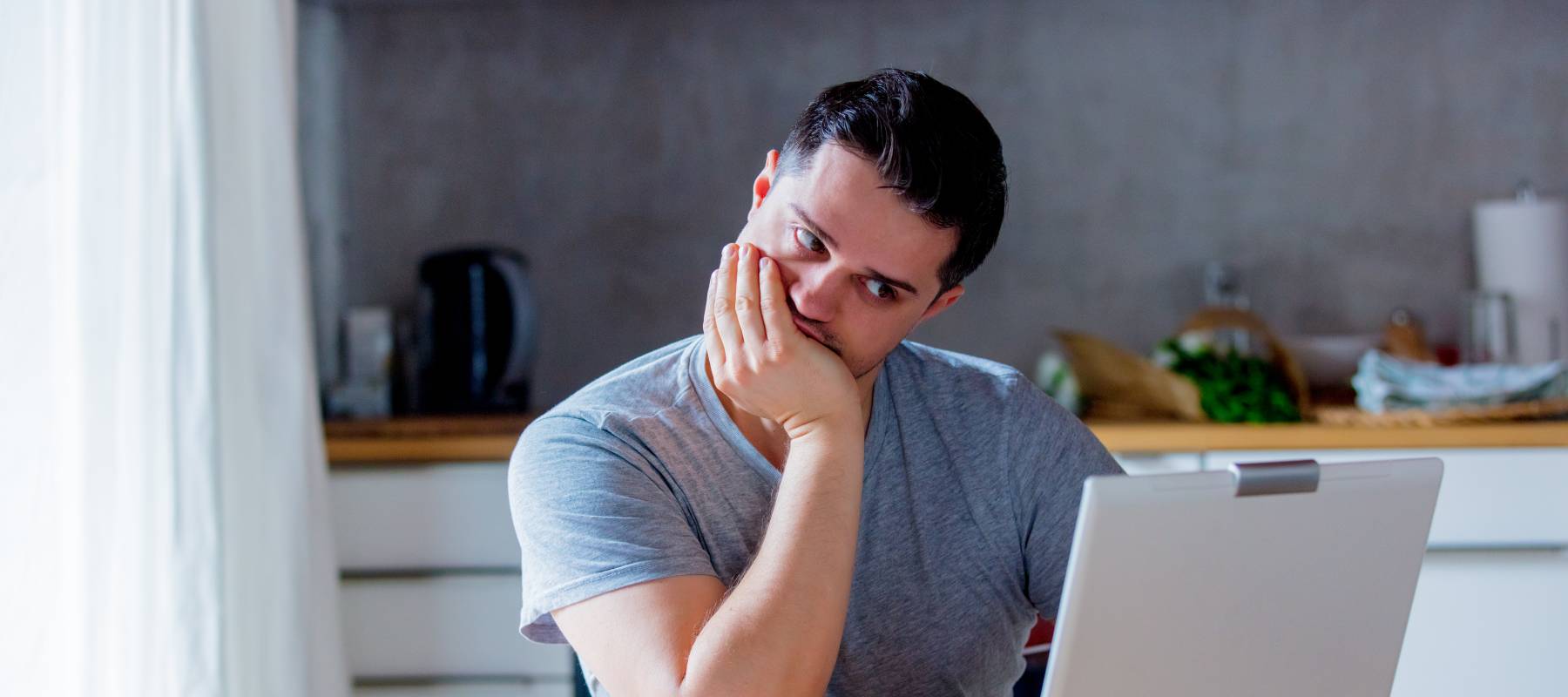 young Caucasian man looking for job in Internet while sitting at kitchen