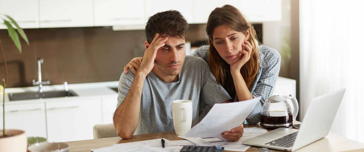 Unhappy American couple managing home accounts in kitchen, trying to save some money by cutting family expenses. Finances, bankruptcy, taxes, money, accounting and financial problems concept