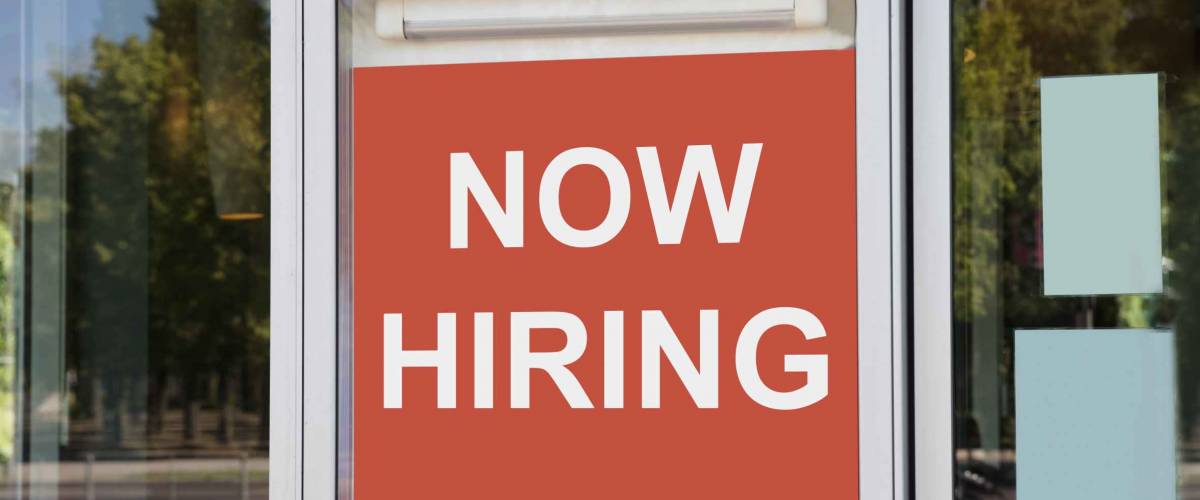 Closeup of now hiring sign outside modern office building