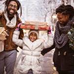 Black family (father, child and mother) bringing home small Christmas tree and packages