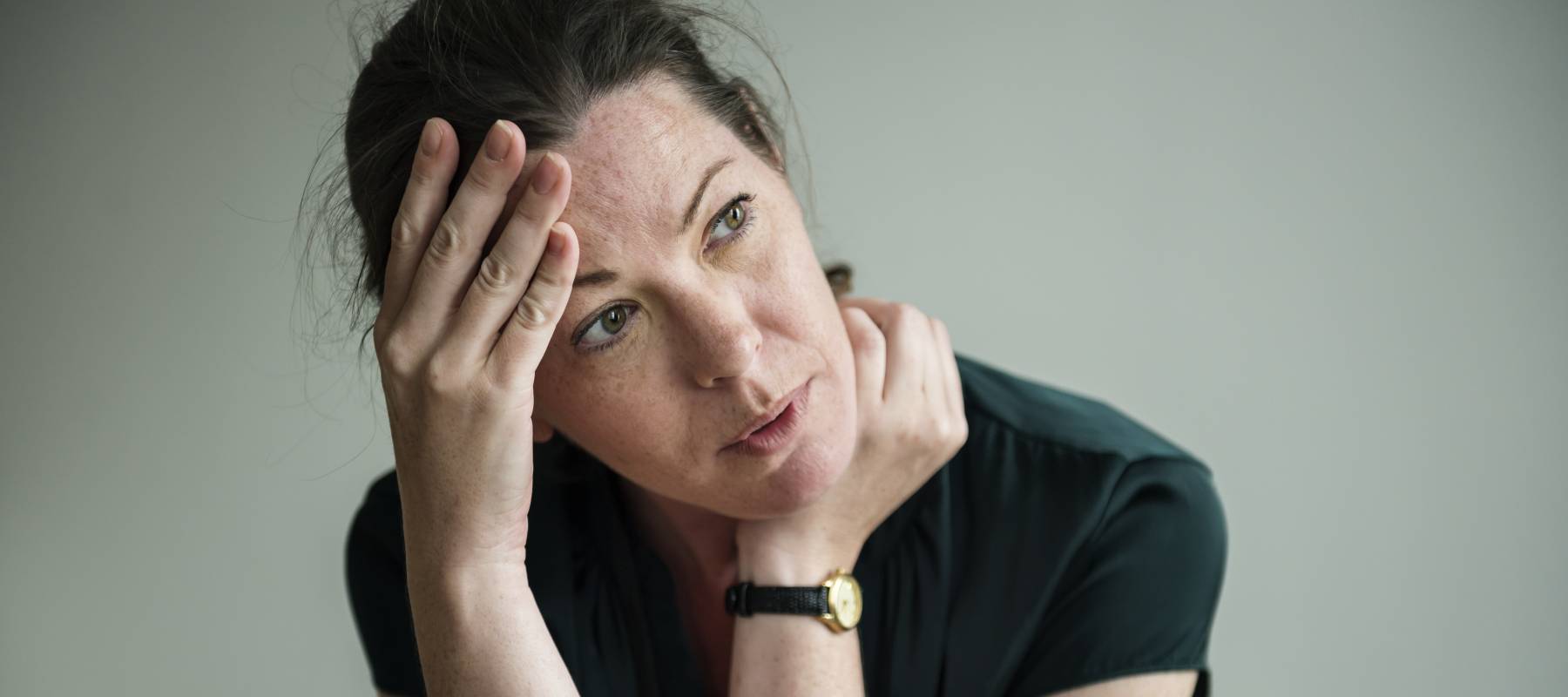 a Caucasian woman looking off-camera, stressed with hand to forehead