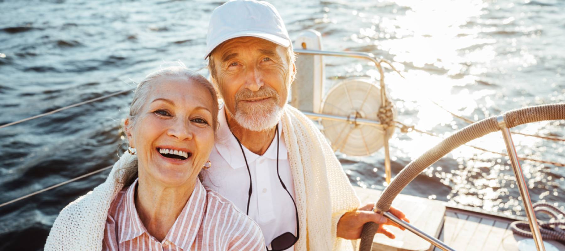senior Caucasian couple sitting at the steering wheel on a sailboat and looking at camera
