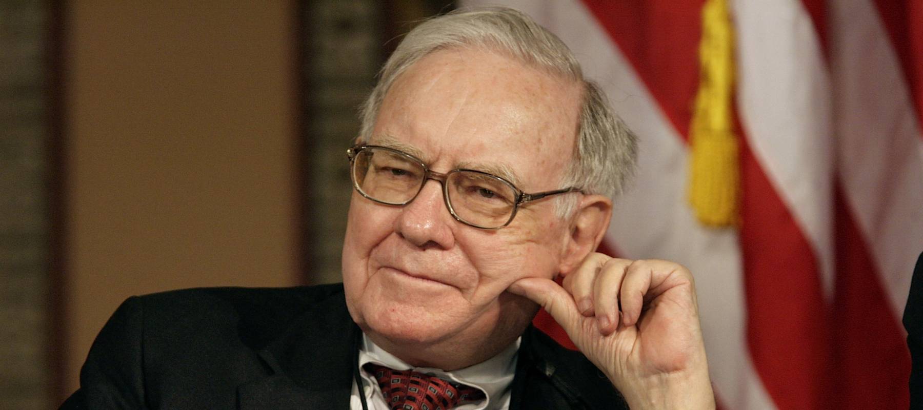 Warren Buffett leans the side of one cheek against his left hand, exposing a gold wrist watch, looking dower.