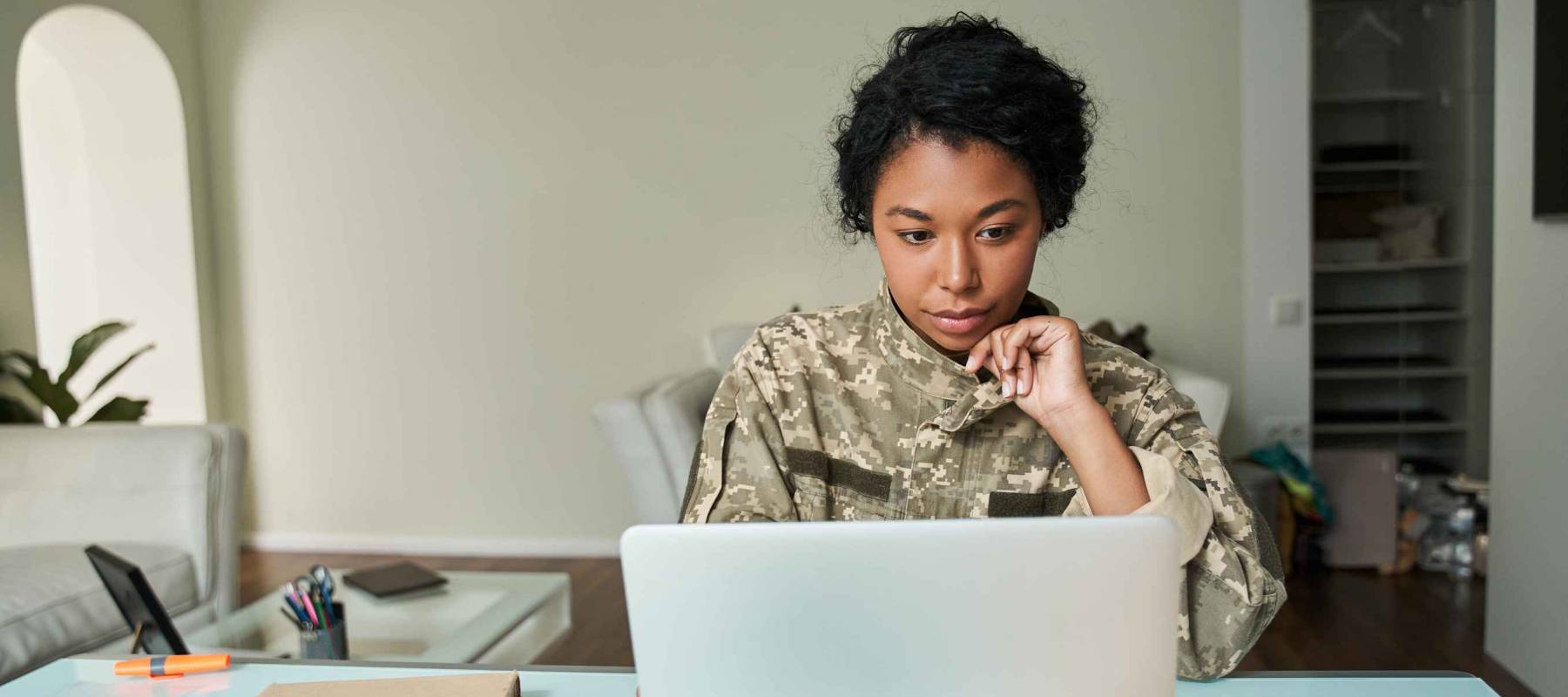 Multiracial soldier woman wearing military uniform looking at the laptop screen