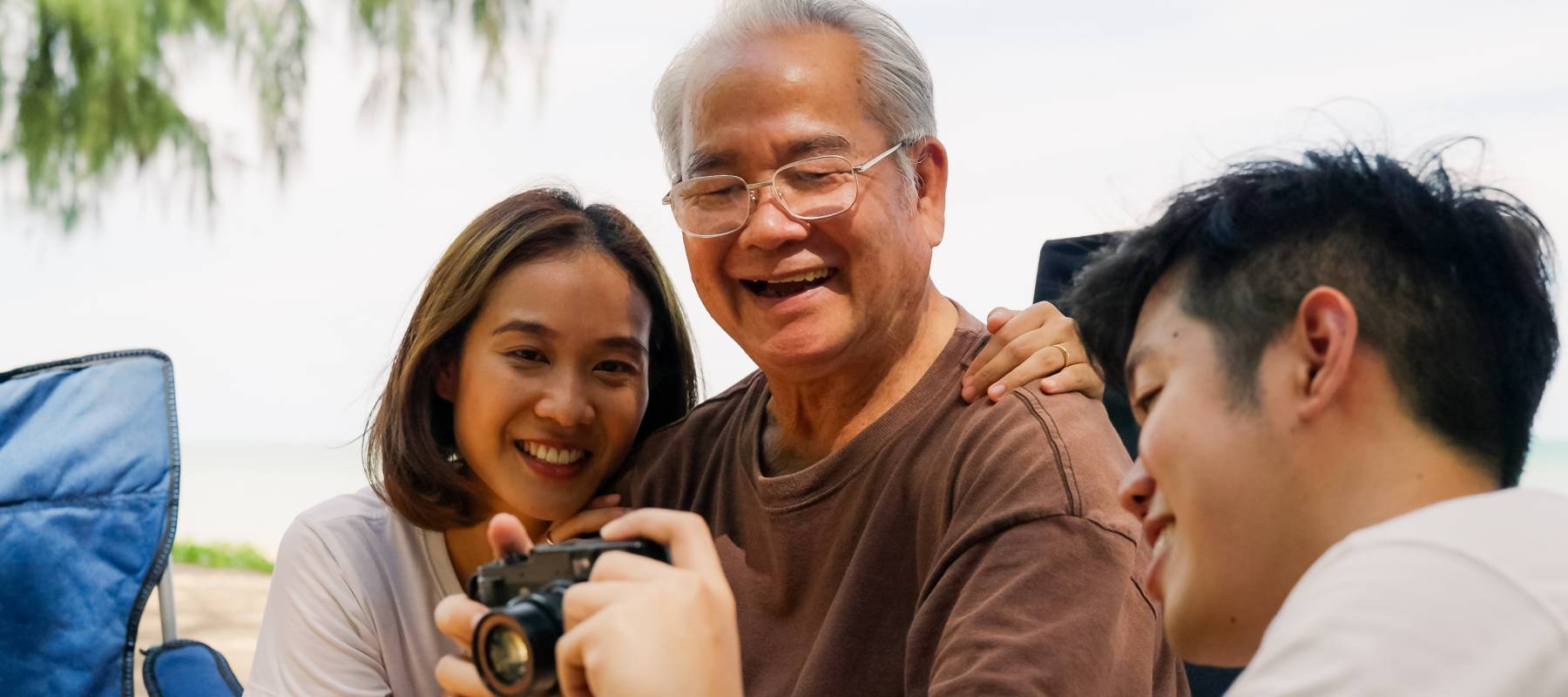 a older Asian man with his two adult kids, laughing together and looking at a camera