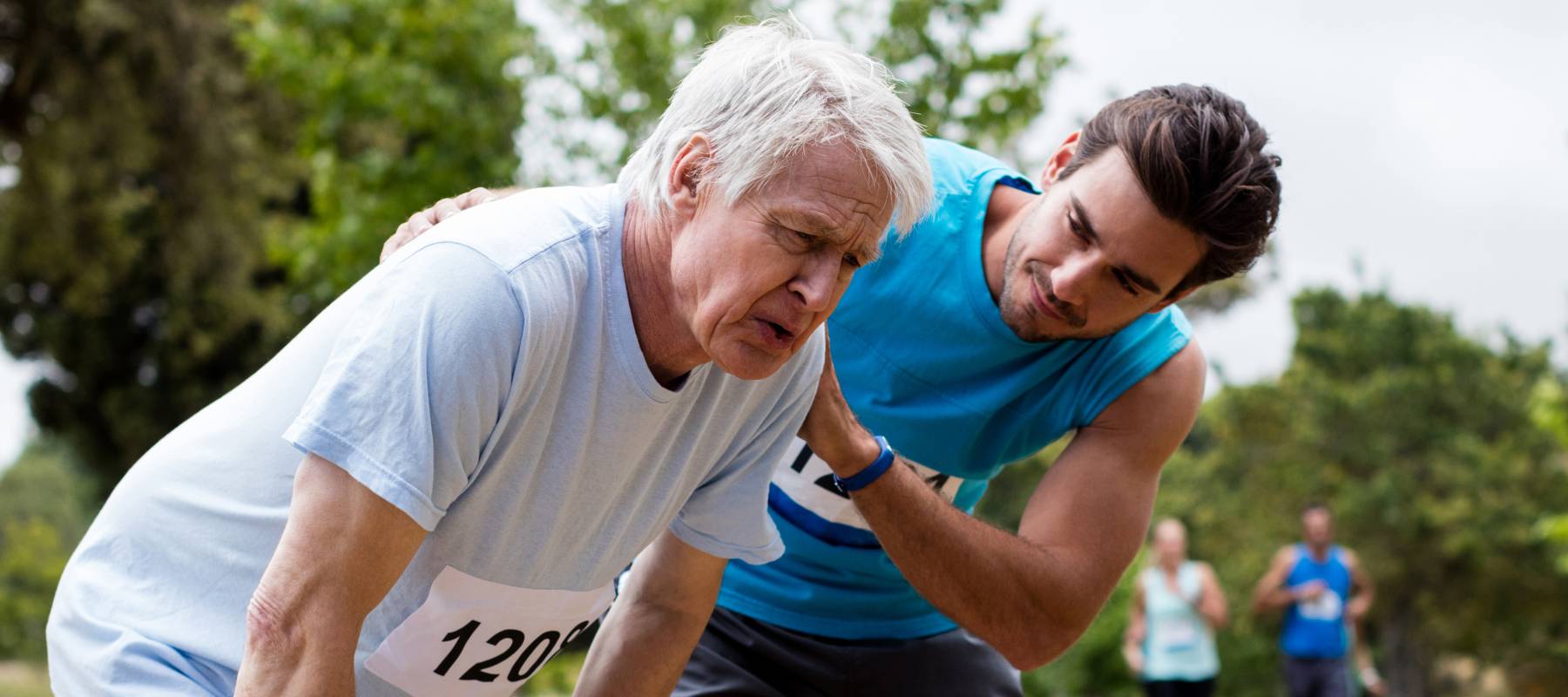 Older man bending over to catch his breath following a race, as a younger man supports him.