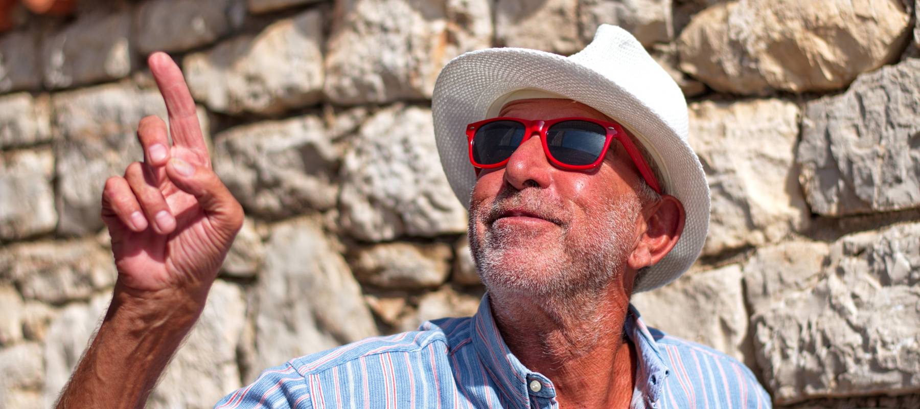 Waist up portrait of a senior man with a hat against the stone wall